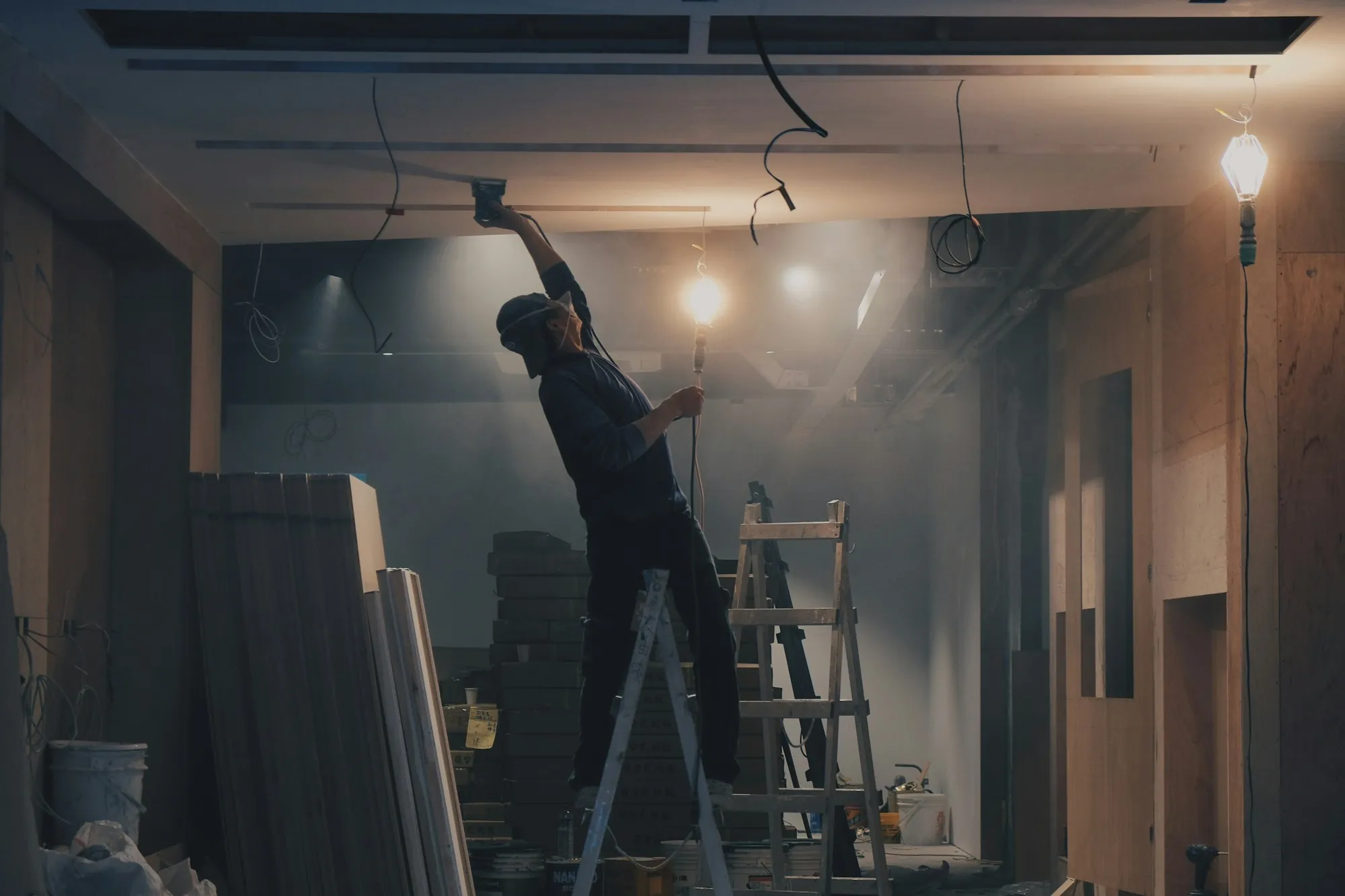 Worker on a ladder installing ceiling wiring inside a framed addition