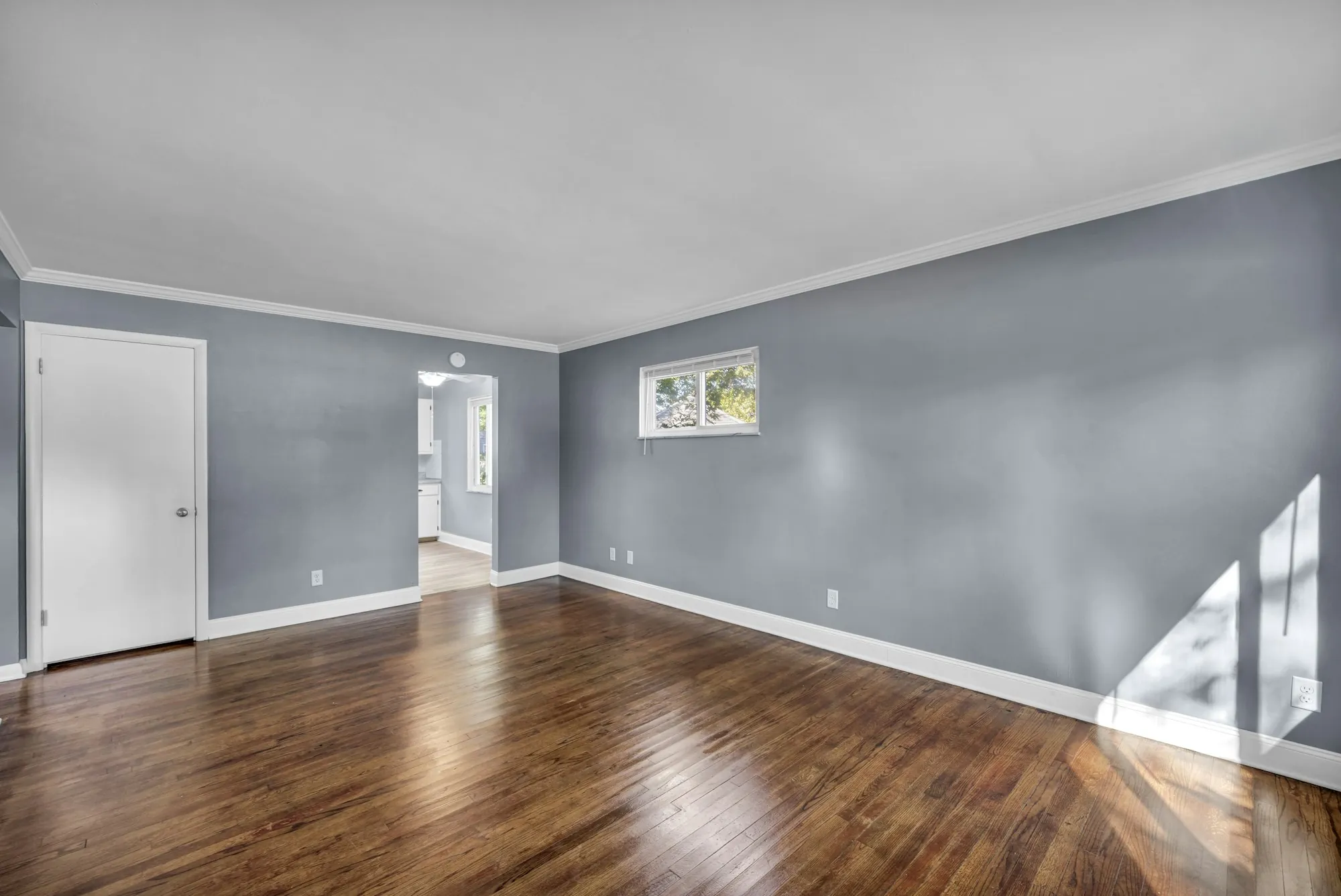 Empty room with freshly painted blue-gray walls, white trim and hardwood floors